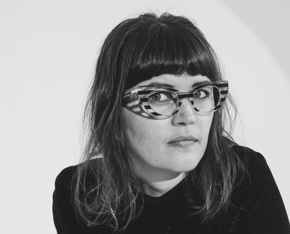 A woman with long hair and striped glasses is gazing intently to the side in a black and white photo.